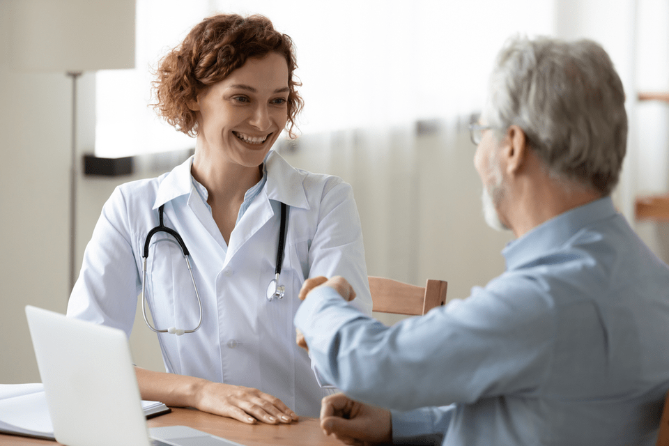 A doctor and senior man talk at a desk.