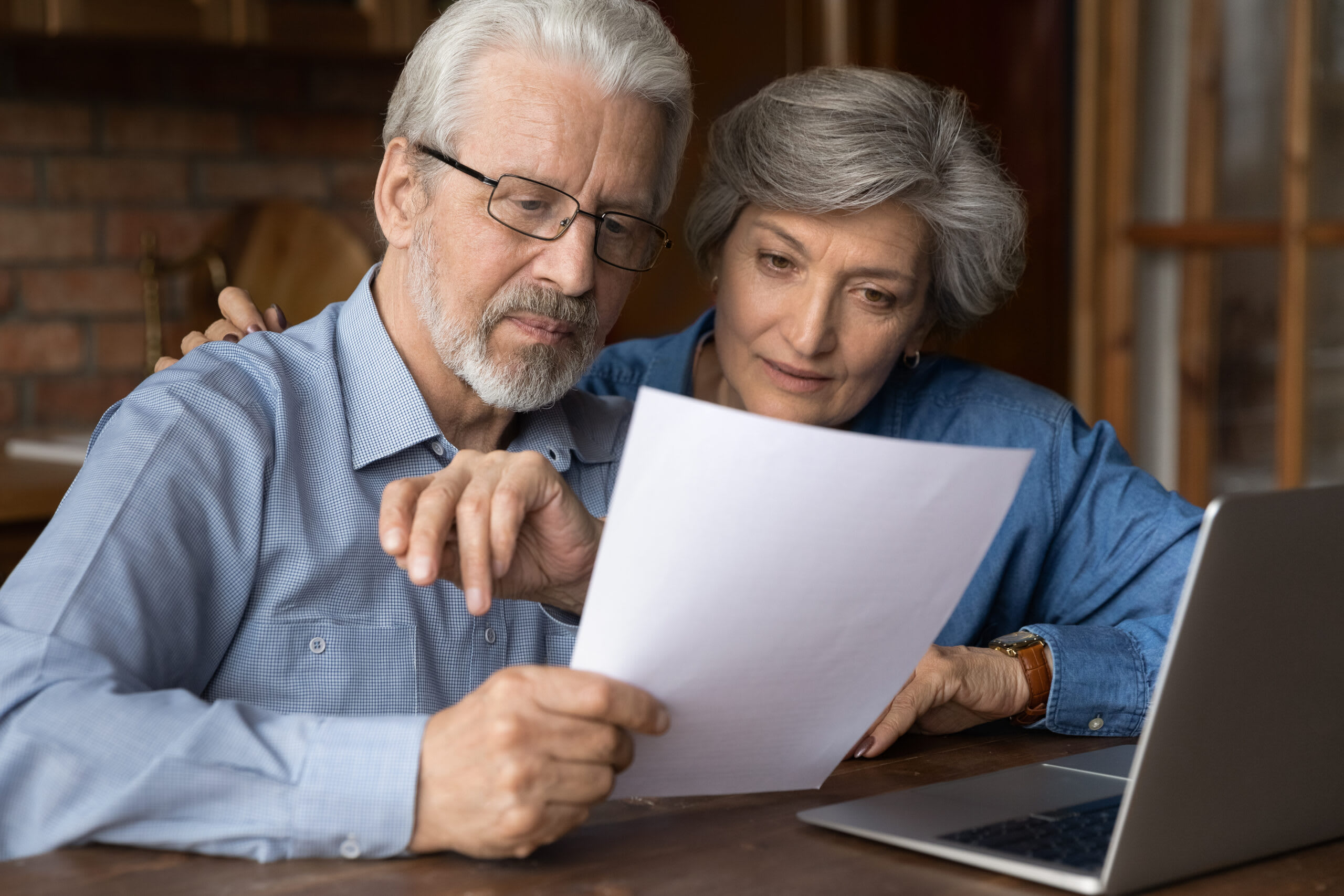 A senior man and woman look at a paper while sitting at a desk.