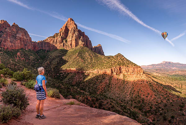 A senior woman looking out across the Southwestern desert at a hot-air balloon